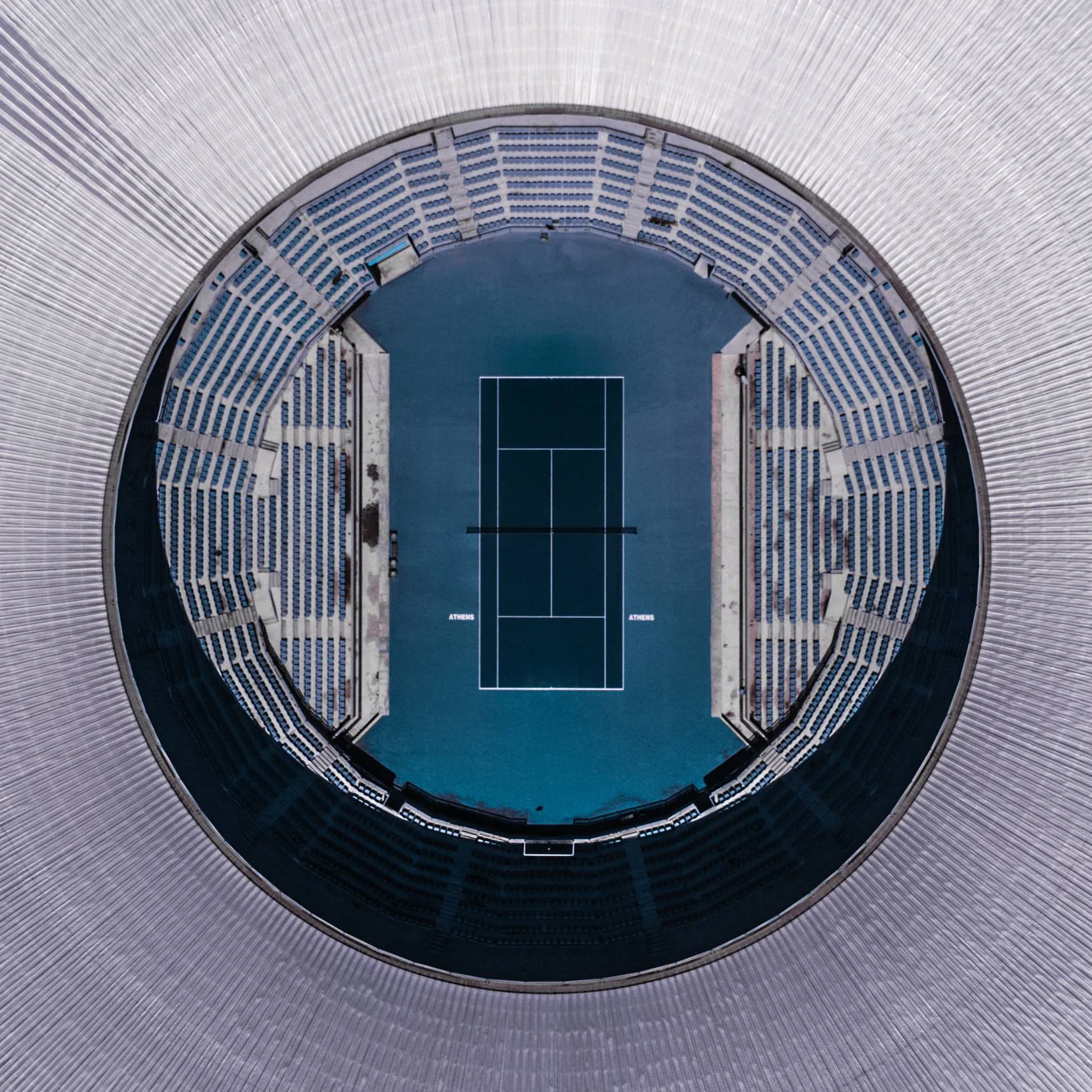 Top-down view of an empty tennis stadium, the blue court framed by the circular roof