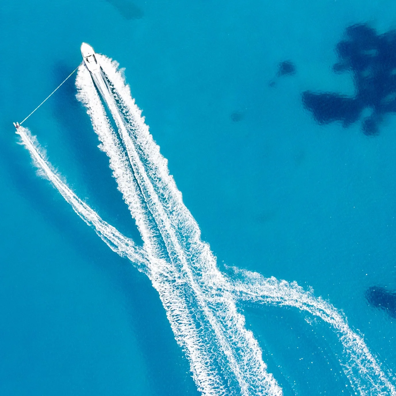 A speedboat towing a water-skier across turquoise sea, their wakes crossing