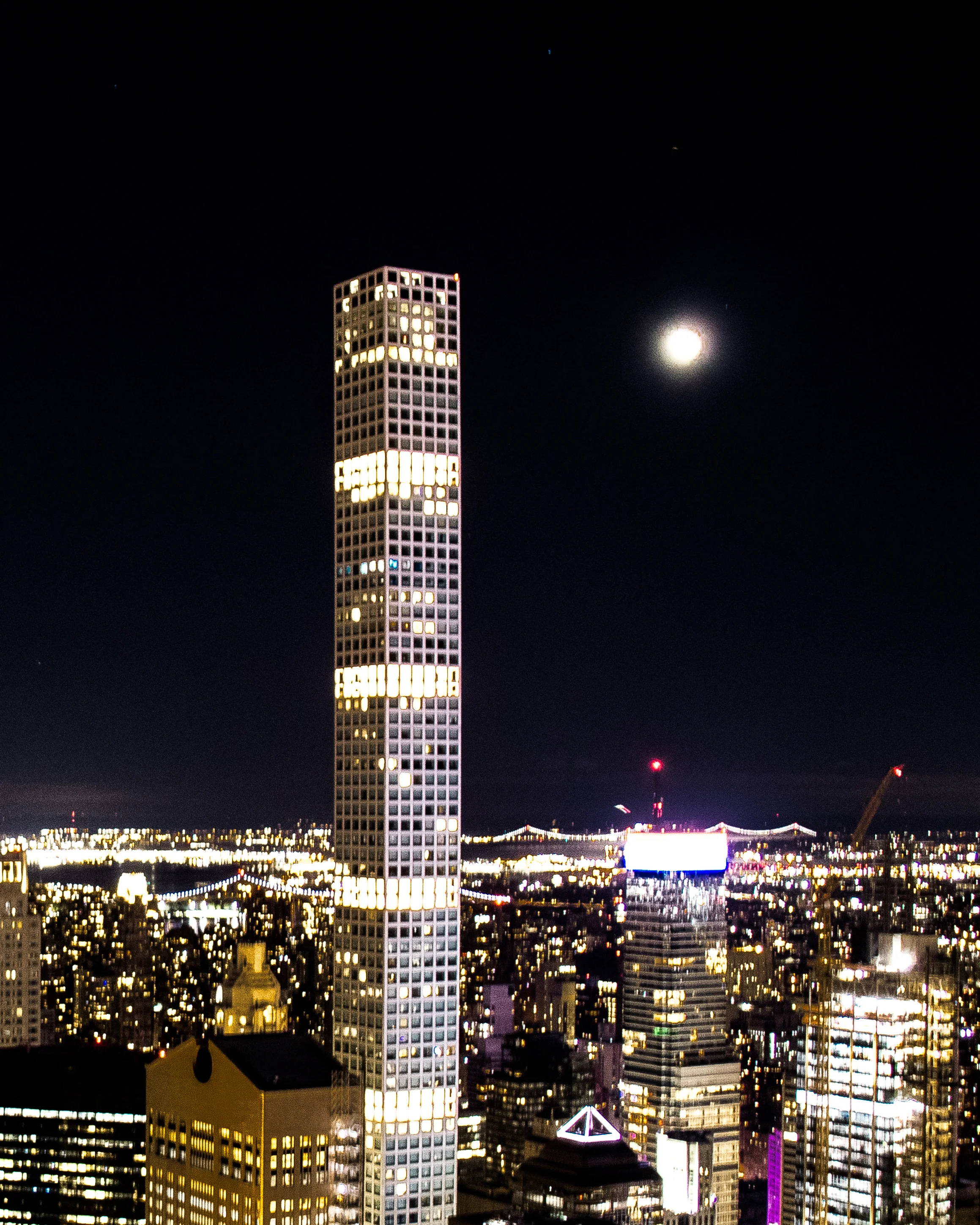 432 Park Avenue lit up at night beside the full moon over Manhattan