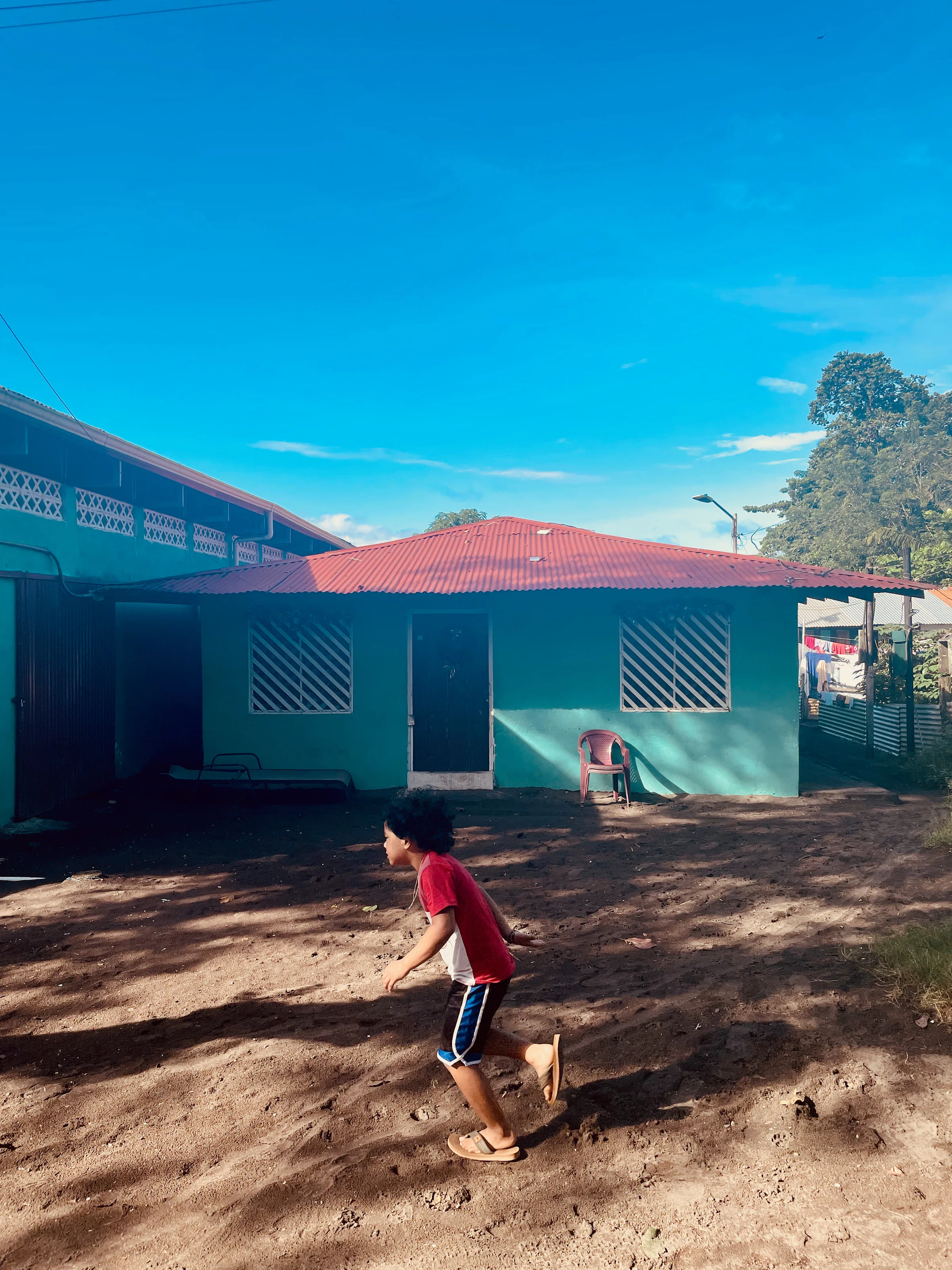 A child running past a turquoise house with a red tin roof